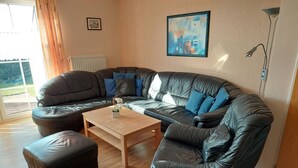 A modern living room with a sectional sofa, a coffee table, and a small ottoman. - Vacation home Mühlenblick 41 No. 3 (Wittmund)