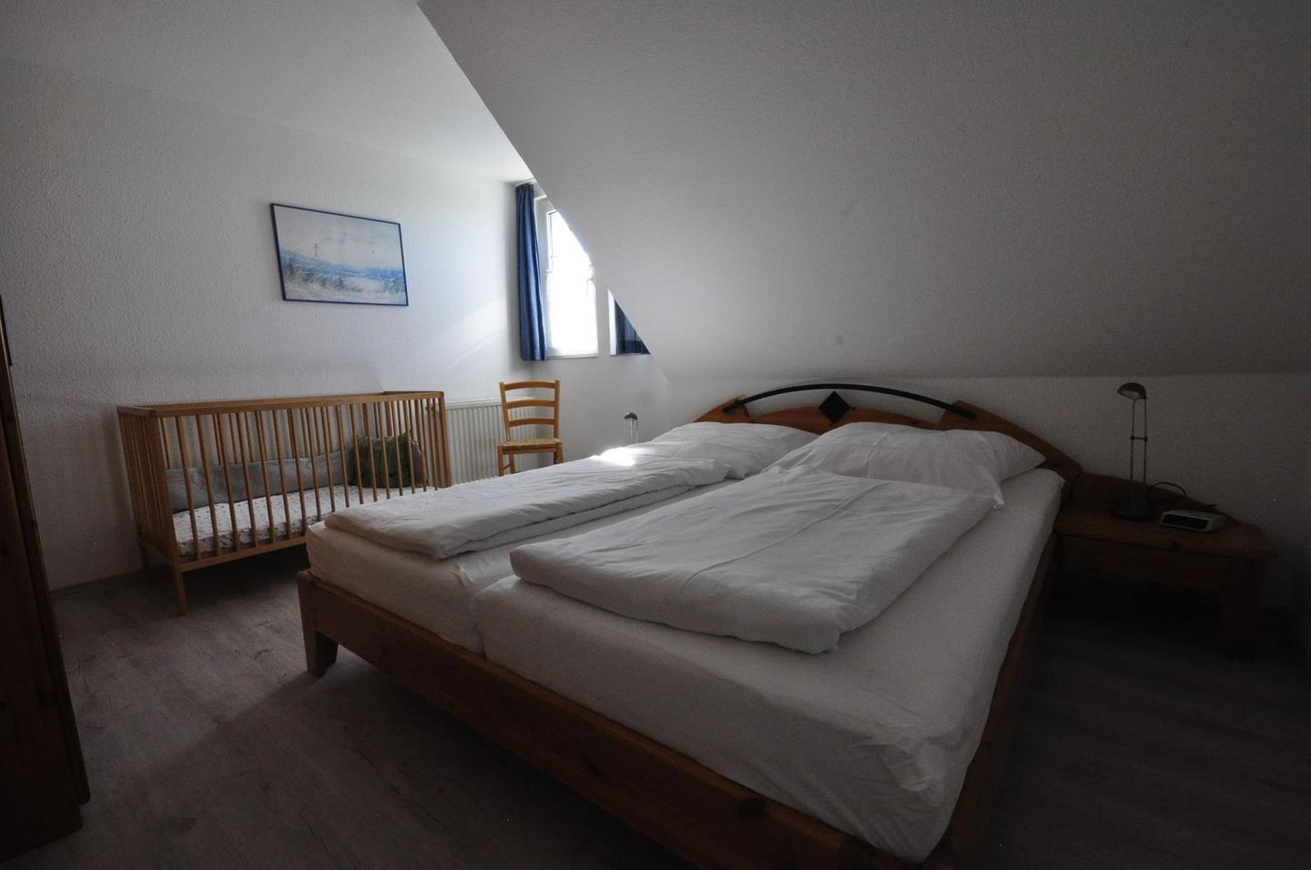 A bedroom with a wooden bed, a crib, a chair, a nightstand, and a lamp.