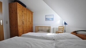 A bedroom with a sloped ceiling, a wooden wardrobe, a crib, and a chair. - Vacation home Mühlenblick 41 No. 3 (Wittmund)