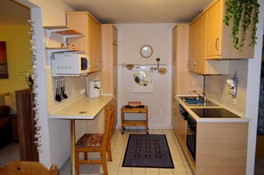 Een compacte keuken met houten kastjes, een magnetron, een koffiezetapparaat en een spoelbak.