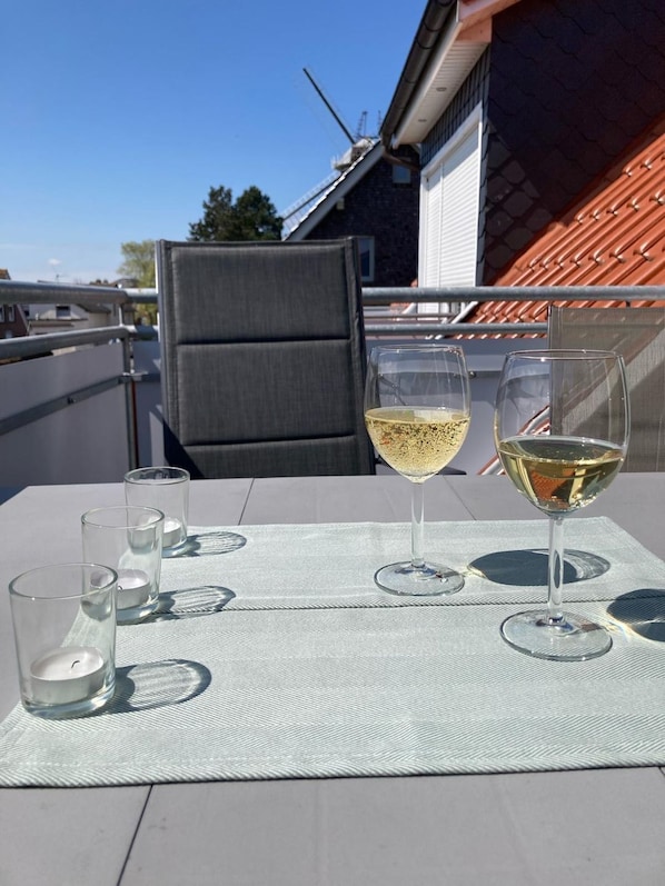 A balcony with a table set for two, two wine glasses, and three empty glasses.