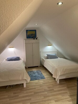 A small, triangular attic bedroom with two single beds, a white wardrobe, and a framed picture on the wall. - Apartment Mühlenstraße 28 Whg. 6 (Wittmund)