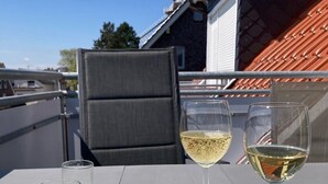 Un balcon avec une table dressée pour deux personnes, deux verres à vin et trois verres vides.