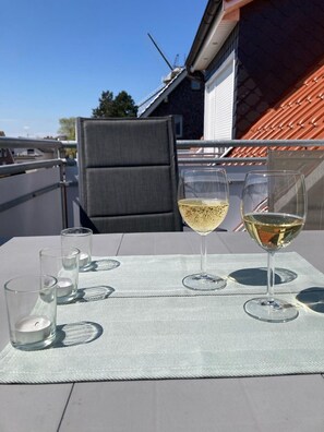 Un balcon avec une table dressée pour deux personnes, deux verres à vin et trois verres vides.
