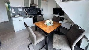 Une cuisine moderne avec des meubles blancs, une table à manger en bois et des chaises recouvertes d’un tissu gris.