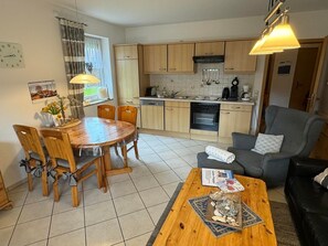 Cocina compacta con armarios de madera, una mesa de comedor con sillas, una mesa baja y un sofá gris.