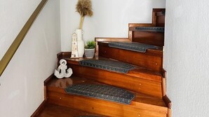 Un escalier en bois avec une rampe, une petite plante décorative et un vase blanc sur le palier.