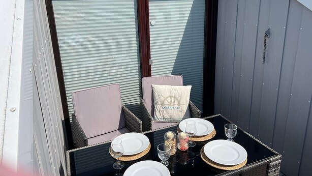Un espace de restauration en plein air avec une table dressée pour quatre personnes, comprenant des assiettes, des verres et une bougie.