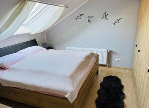 A bedroom with a bed, a window with curtains, a radiator, and wall art of birds. - Ferienwohnung Schollenpadd 11 OG (Wittmund)