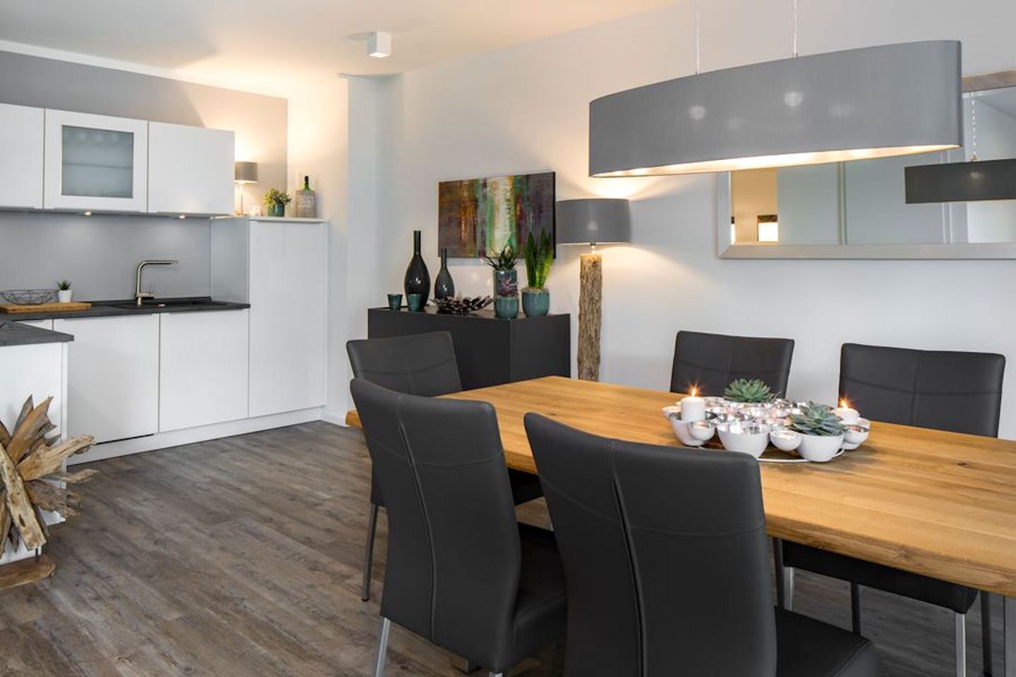 A modern kitchen with white cabinets, a wooden dining table with black chairs, and a painting on the wall.
