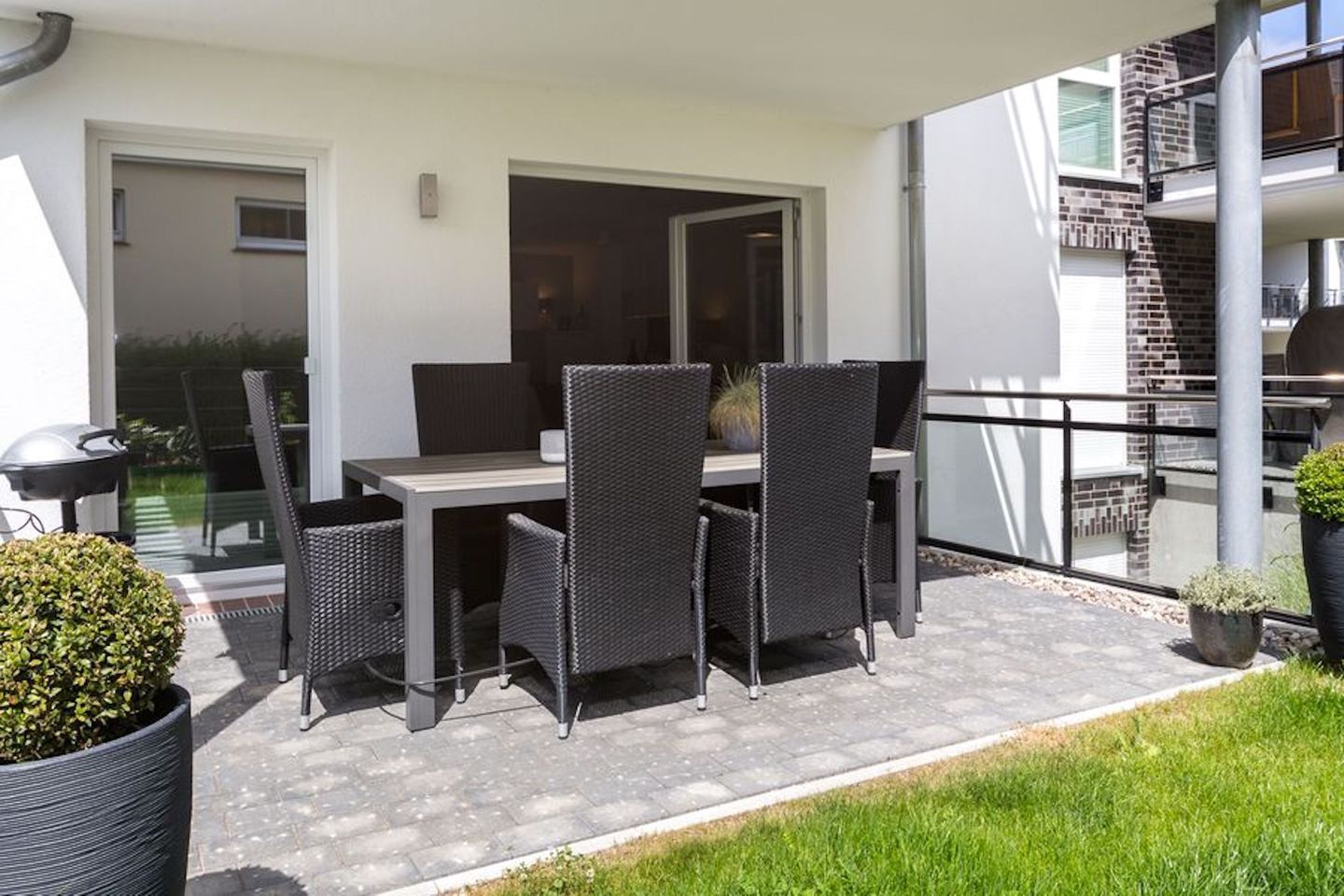 Um pátio externo com mesa, cadeiras, churrasqueira e plantas em vasos.