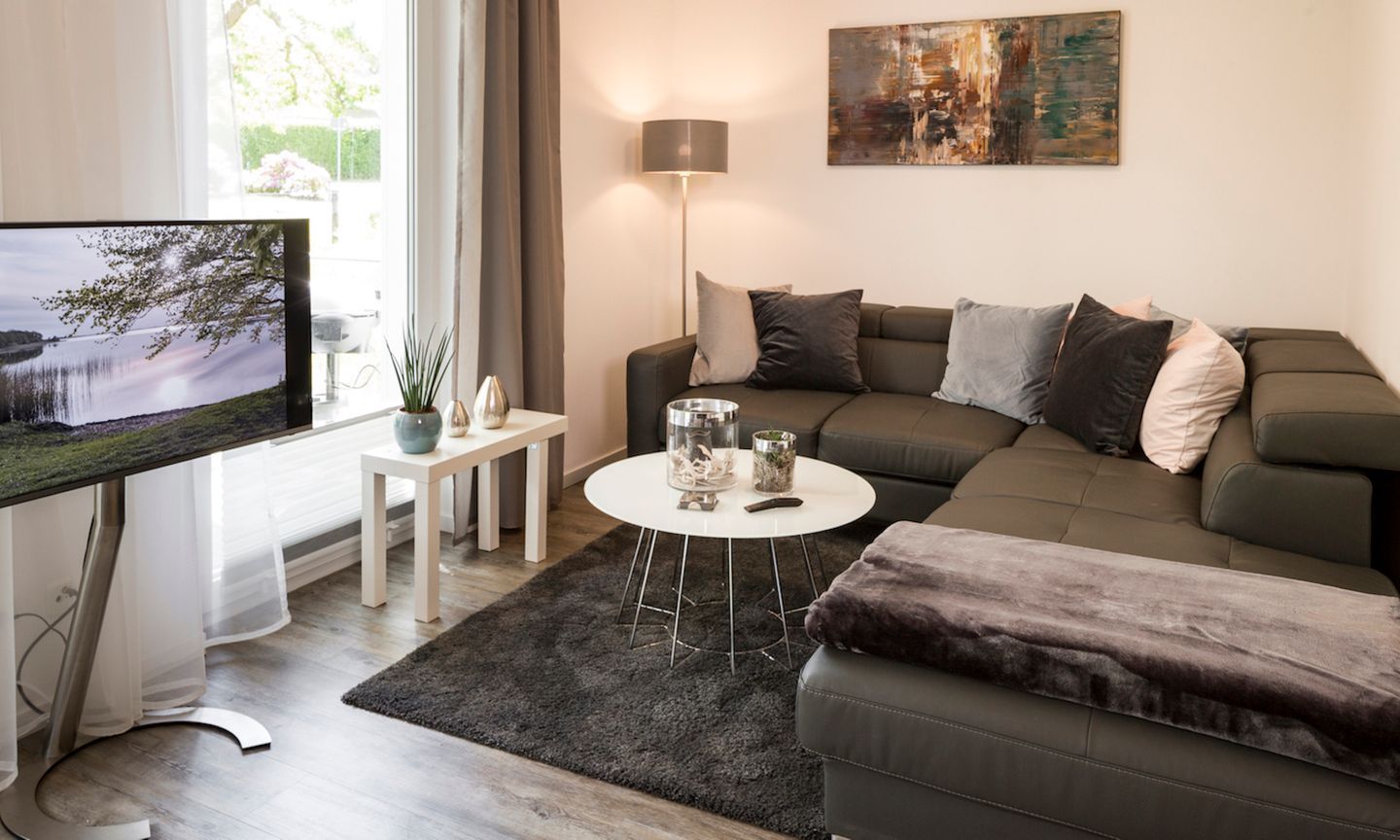 A modern living room with a grey sofa, a round coffee table, and a flat-screen TV on a stand.