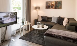 Ein modernes Wohnzimmer mit einem grauen Sofa, einem runden Couchtisch und einem Flachbildfernseher auf einem Lowboard.