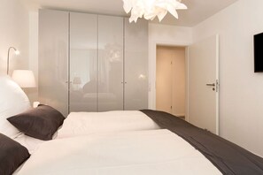 Quarto com cama grande, guarda-roupa, abajur e televisão na parede.