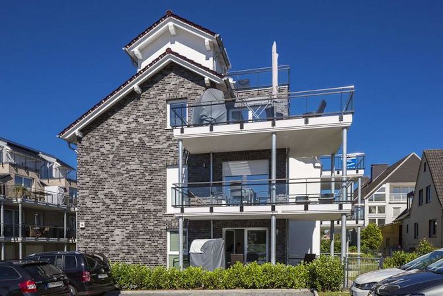 A modern two-story building with a stone facade, balconies, and a clear blue sky.