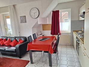 A modern kitchen with a red table and chairs, a clock on the wall, and a view of the outside.