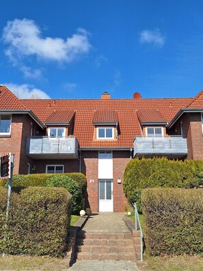 A multi-story residential building with a red-tiled roof, brick facade, and a central entrance.