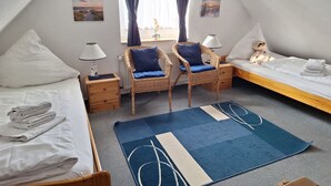 Ein Zimmer mit einem Bett, zwei Stühlen, einem kleinen Tisch, einem Nachttisch und einem Fenster mit Vorhängen.