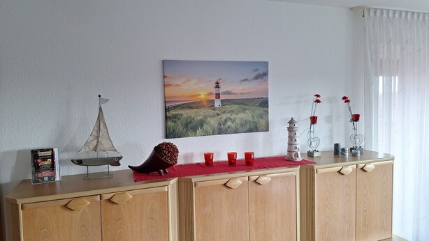 Ein Holzkabinett mit einem Gemälde von einem Leuchtturm, dekorativen Gegenständen und einem kleinen Segelbootmodell.