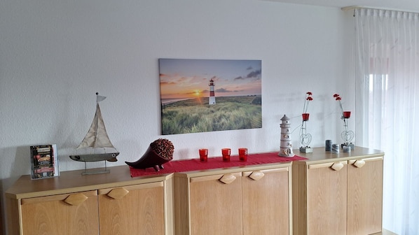 A wooden cabinet with a painting of a lighthouse, decorative items, and a small sailboat model.