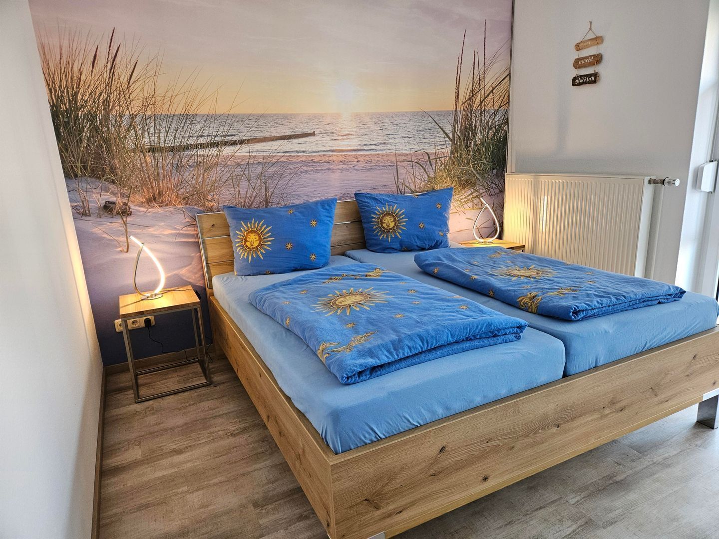 Ein Schlafzimmer mit einem hölzernen Bett, blauer Bettwäsche und einem Wandbild mit Strandmotiv.