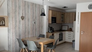 A modern kitchen with wooden cabinets, a dining table with chairs, and a sofa in a living area. - Vacation cottage Mittelweg 41a (Wittmund)