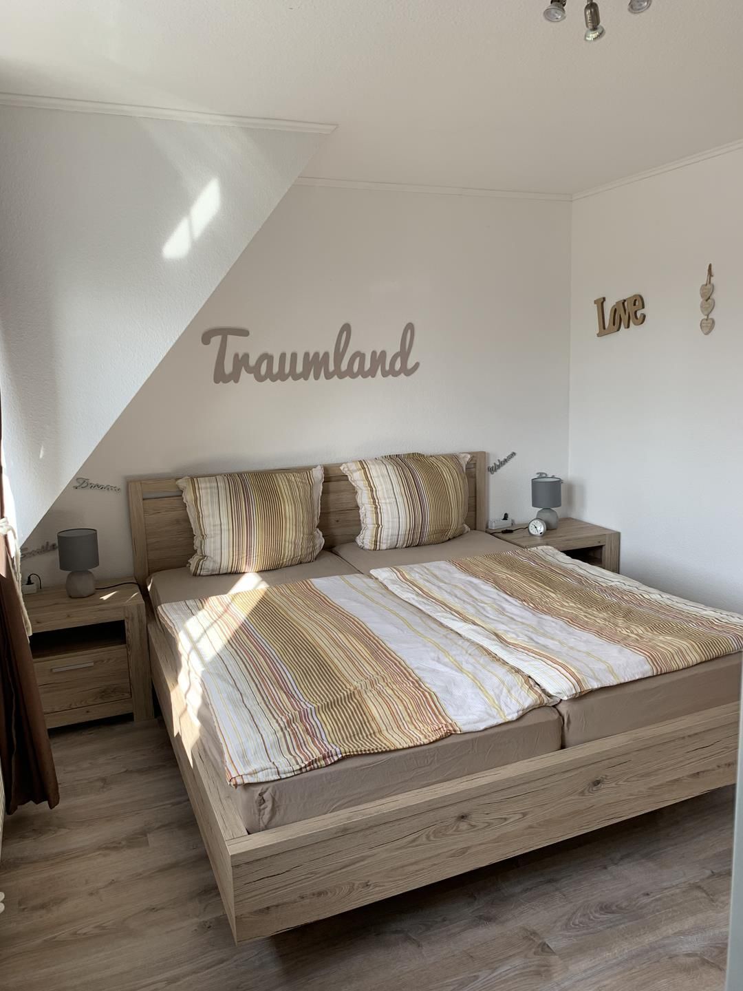 A bedroom with a bed, two nightstands, a lamp, and a wall with 'Trauland' and 'Love' decorations.