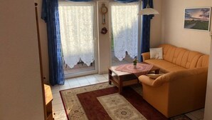 A living room with a sofa, a table with a vase, a patterned rug, and a window with curtains.