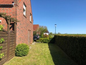 A brick house with a wooden gate, a hedge, and a car parked in the driveway.
