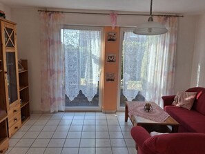 A living room with a red sofa, a wooden cabinet, and a table with a lace tablecloth. - Vacation Home “Am Kurzentrum 6” (Wittmund)
