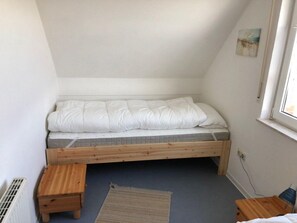 A small, single-bed room with a sloped ceiling, a window, and a radiator.