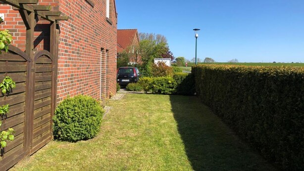 A brick house with a wooden gate, a hedge, and a car parked in the driveway.