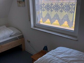 A bedroom with a single bed, a window with a decorative screen, and a small wooden table.