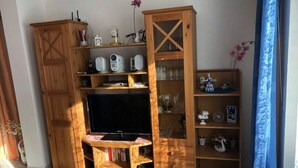 A wooden entertainment unit with a flat-screen TV, shelves with decorative items, and a small table with a pink mat.