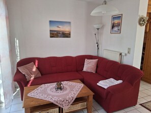 A red sofa with a lace tablecloth and a small basket, a white lamp, and two framed pictures on the wall.