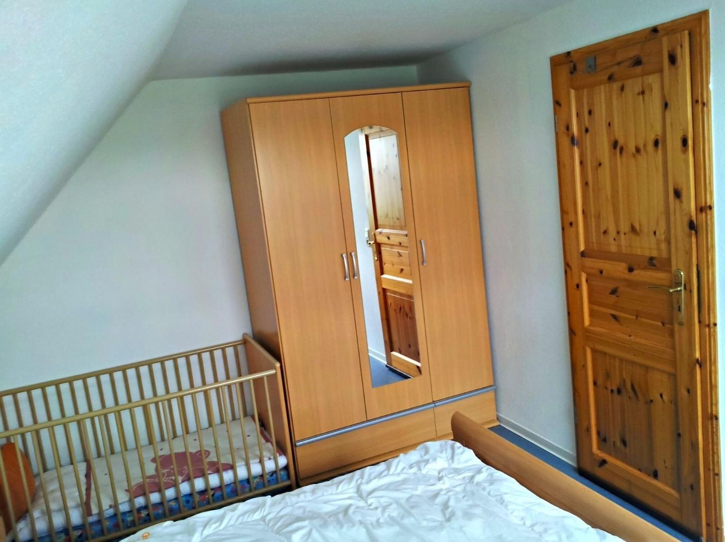 Une chambre à coucher avec une armoire en bois, un berceau et un grand miroir.