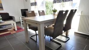 Zona de menjador amb taula rectangular, sis cadires i un televisor al fons.