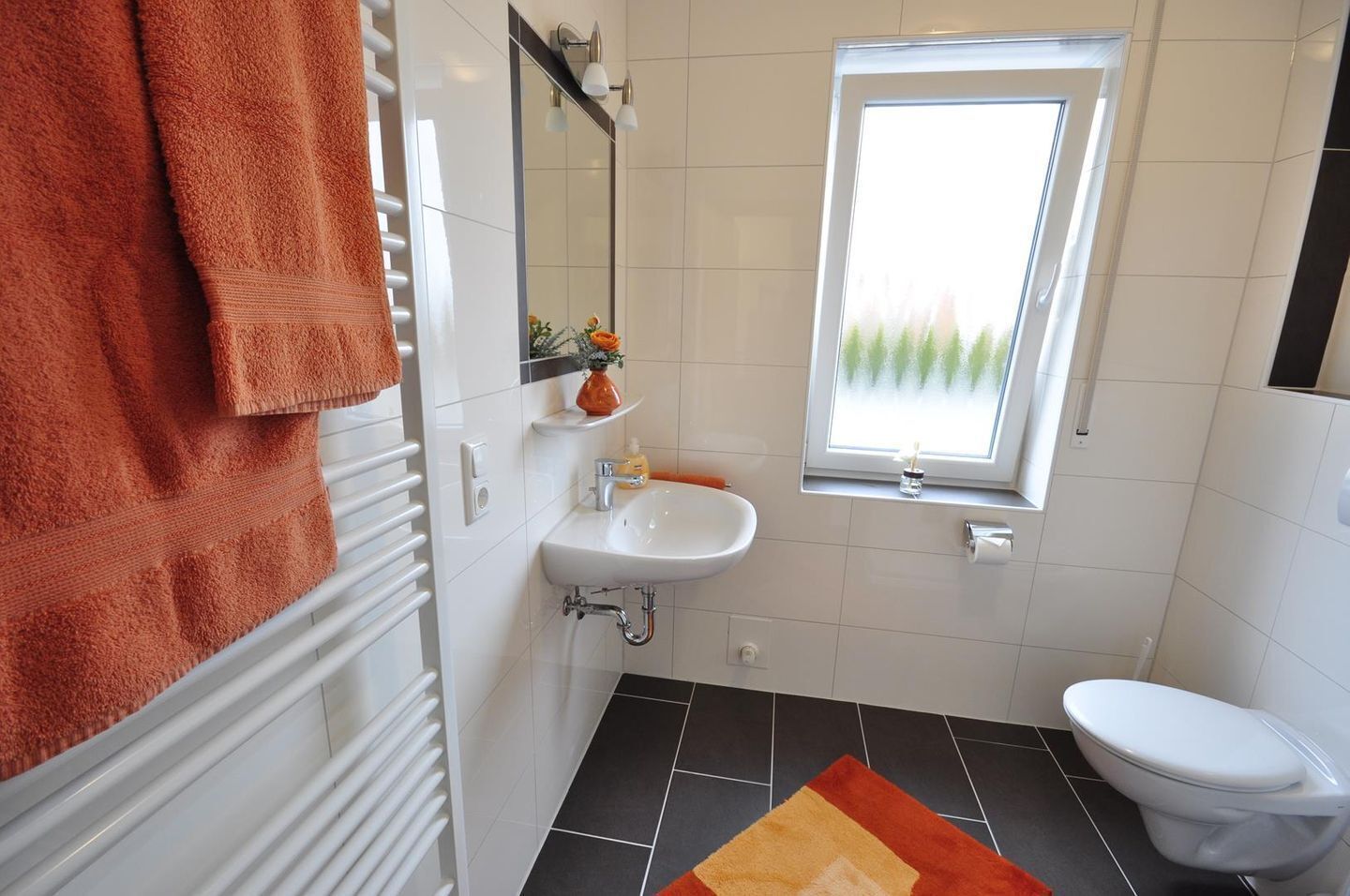 A bathroom with a white sink, a toilet, a towel rack with a towel, a mirror, and a window with a view of trees.