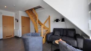 Ein modernes Wohnzimmer mit einer Holztreppe, einem grauen Sofa und einem blauen Sessel.