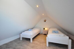 Un dormitorio pequeño y blanco estilo ático con dos camas individuales, una mesita de noche y una lámpara en el techo.