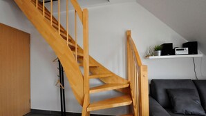 Ein modernes Wohnzimmer mit einer Holztreppe, einem schwarzen Sofa und einer weißen Wand mit Regal.
