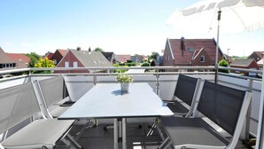 Eine Dachterrasse mit Tisch, Stühlen, einer Topfpflanze und einem großen Sonnenschirm.