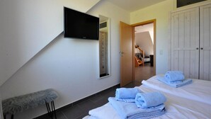 Ein Hotelzimmer mit Flachbildfernseher an der Wand, einer Holztür, die zu einer Treppe führt, und einem Schrank mit Spiegel.