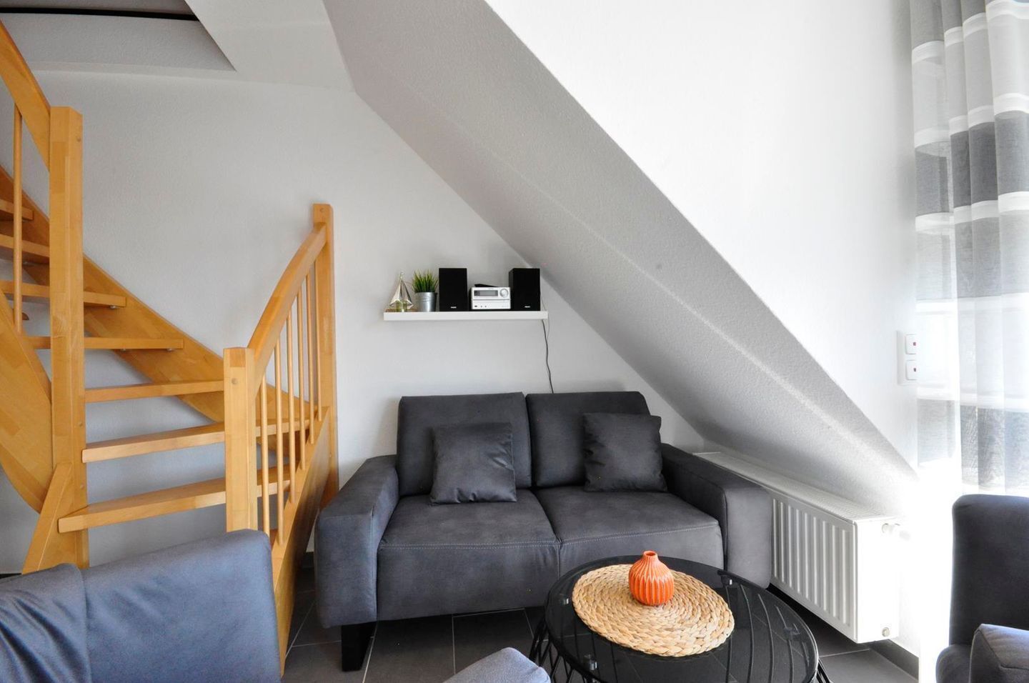 A modern loft with a grey sofa, wooden staircase, and a white radiator.