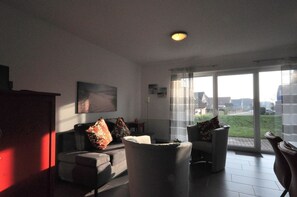 A modern living room with a sofa, armchairs, and a coffee table. There is a large window with a view of the outside. - Residence Carolinensiel Mühlenstraße 28 Whg. 3 - Residence Carolinensiel 1 (Wittmund)