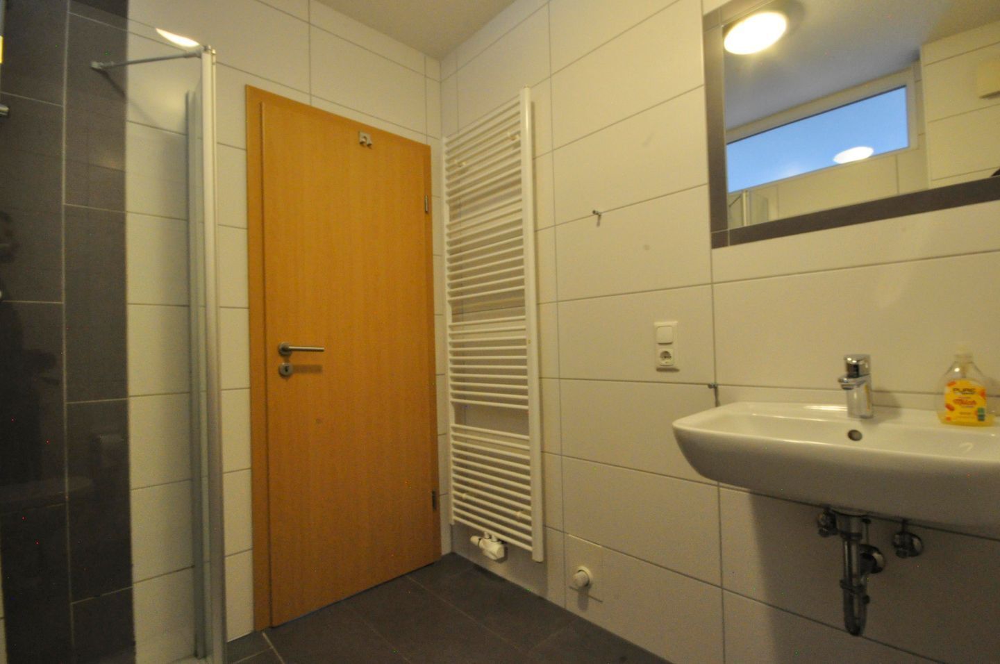 A bathroom with a wooden door, a white sink, and a mirror above it.