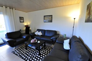 Un salon avec un canapé en cuir noir, une table basse sur laquelle sont posés des livres et une théière, et un tapis à pois.