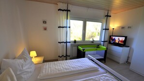 A bedroom with two beds, a television, a desk, and a window with curtains.
