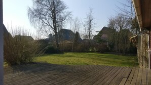 A wooden deck with a grassy lawn and leafless trees in the background.