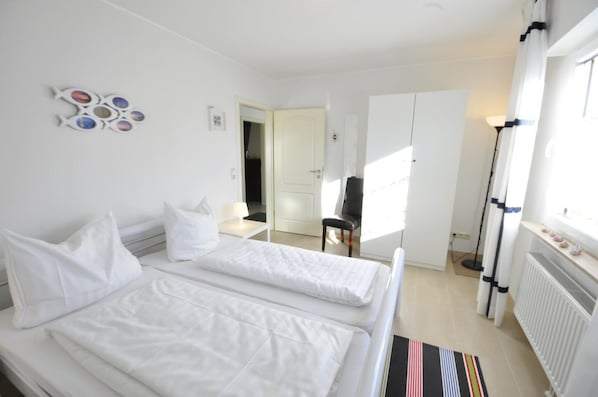 Une chambre d’hôtel avec deux lits, une chaise, un radiateur et une fenêtre avec des rideaux.